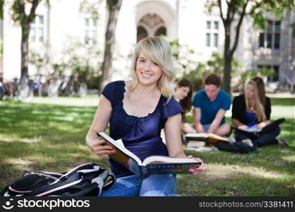 Portrait of smiling young girl with book with her classmates studying in background