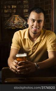 Portrait of smiling young Hispanic man holding beer in pub.