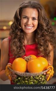 Portrait of smiling young housewife holding christmas decorated plate with oranges