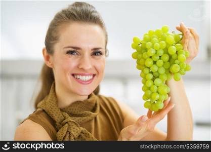 Portrait of smiling young housewife showing branch of grapes