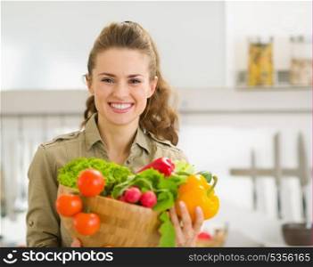 Portrait of smiling young housewife showing plate of fresh vegetables