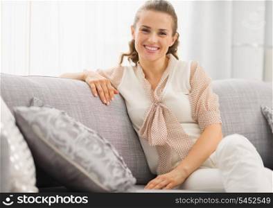 Portrait of smiling young housewife sitting on couch in living room