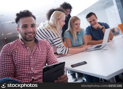 Portrait of smiling young informal businessman with colleagues in background at the office