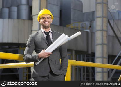 Portrait of smiling young male architect holding blueprints outside building