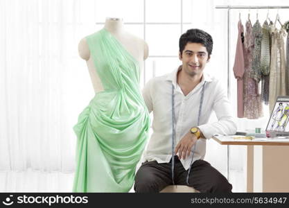 Portrait of smiling young male fashion designer with dressmaker&rsquo;s dummy