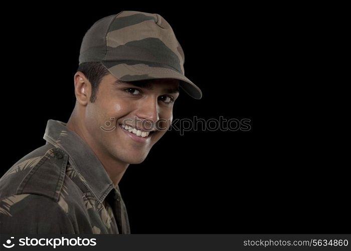 Portrait of smiling young male soldier against black background