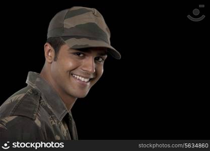 Portrait of smiling young male soldier against black background