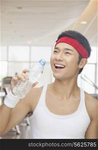 Portrait of smiling young man drinking from water bottle at the gym