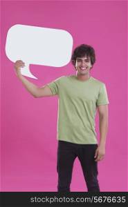 Portrait of smiling young man holding speech bubble over pink background