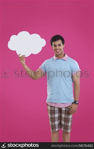 Portrait of smiling young man holding thought bubble over pink background
