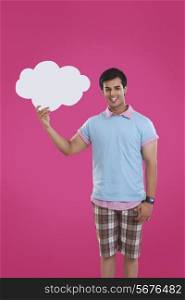 Portrait of smiling young man holding thought bubble over pink background