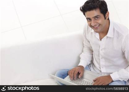 Portrait of smiling young man on sofa with laptop