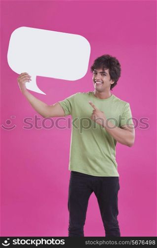Portrait of smiling young man pointing at speech bubble over pink background