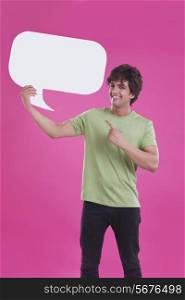 Portrait of smiling young man pointing at speech bubble over pink background