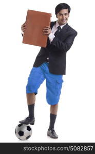 Portrait of smiling young man standing with his one foot on a football and holding briefcase