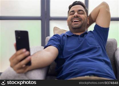Portrait of smiling young man using  Mobile Phone while sitting on sofa at home