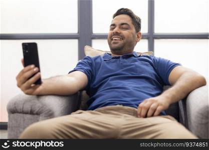 Portrait of smiling young man using  Mobile Phone while sitting on sofa at home