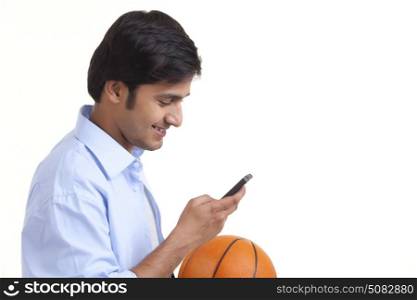 Portrait of smiling young man with basket ball using mobile phone