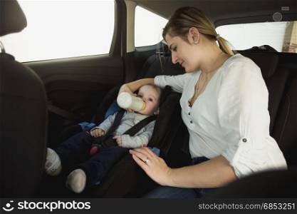 Portrait of smiling young mother feeding baby boy in car