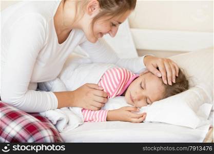 Portrait of smiling young mother holding hand on sleeping daughters head