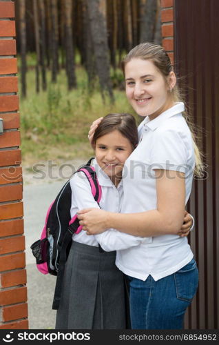 Portrait of smiling young mother hugging her daughter before seeing her off to school