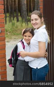 Portrait of smiling young mother hugging her daughter before seeing her off to school