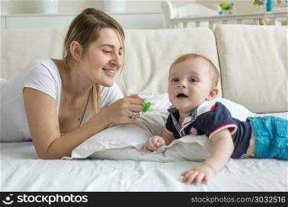 Portrait of smiling young mother with her baby boy lying on bed. Smiling young mother with her baby boy lying on bed