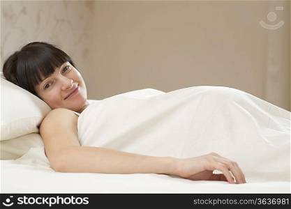 Portrait of smiling young pregnant woman lying on bed