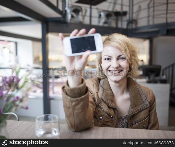 Portrait of smiling young woman displaying cell phone in cafe