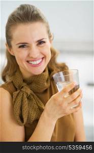 Portrait of smiling young woman drinking water in kitchen