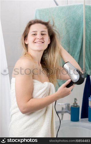 Portrait of smiling young woman drying long hair at bathroom