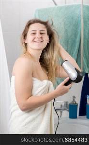 Portrait of smiling young woman drying long hair at bathroom