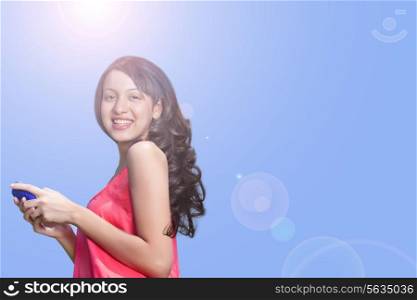 Portrait of smiling young woman holding cell phone against sky