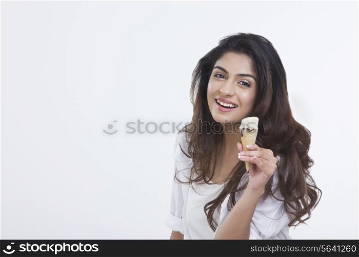 Portrait of smiling young woman holding ice-cream cone over white background