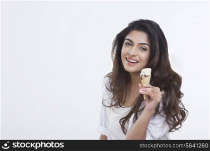 Portrait of smiling young woman holding ice-cream cone over white background
