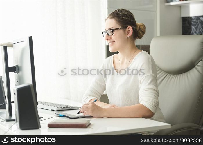 Portrait of smiling young woman in eyeglasses working in office and using graphic tablet. Portrait of smiling woman in eyeglasses working in office and using graphic tablet