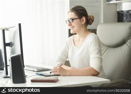 Portrait of smiling young woman in eyeglasses working in office and using graphic tablet. Portrait of smiling woman in eyeglasses working in office and using graphic tablet