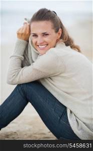 Portrait of smiling young woman in sweater sitting on lonely beach