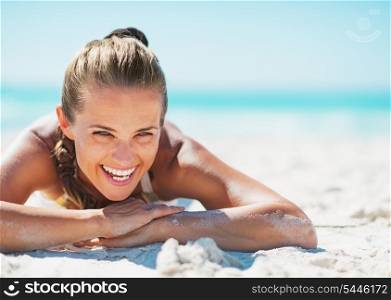 Portrait of smiling young woman in swimsuit laying on beach