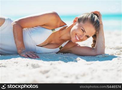 Portrait of smiling young woman in swimsuit laying on beach