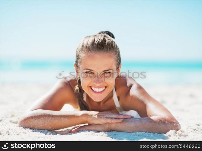 Portrait of smiling young woman in swimsuit laying on sandy beach