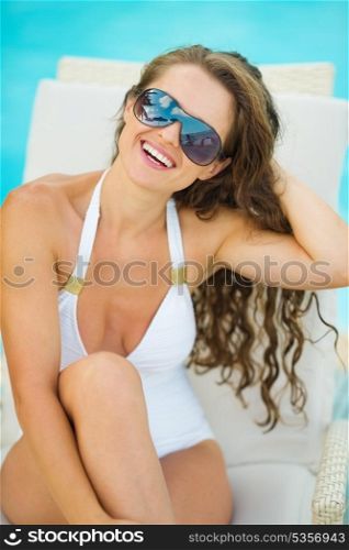 Portrait of smiling young woman in swimsuit relaxing on chaise-longue