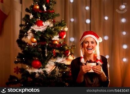 Portrait of smiling young woman near Christmas tree with present box&#xA;
