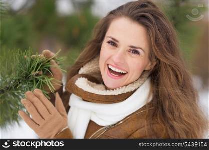 Portrait of smiling young woman near fir-tree in winter park
