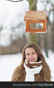 Portrait of smiling young woman standing under bird feeder in winter park