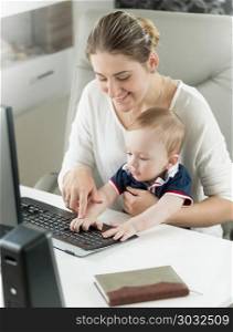 Portrait of smiling young woman teaching her baby son using computer at office. Portrait of smiling woman teaching her baby son using computer at office