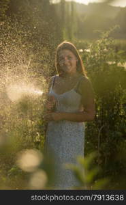 Portrait of smiling young woman watering garden with hose pipe