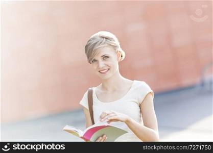 Portrait of smiling young woman with book at campus