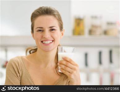 Portrait of smiling young woman with glass of milk in kitchen