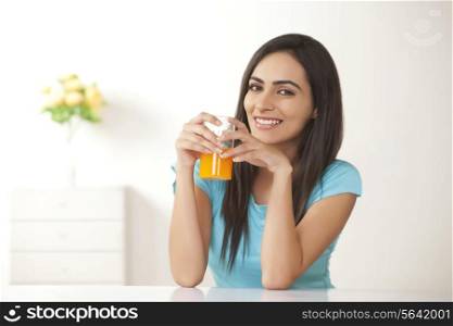 Portrait of smiling young woman with glass of orange juice at home